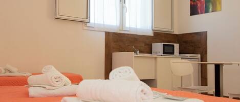 Habitación de hotel con cama, escritorio, silla, microondas y un cuadro de pimientos en la pared.