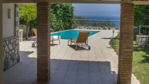 A covered patio area with a pool, lounge chairs, and a view of the ocean. - Corinthian Residence (Xylokastro-Evrostina)