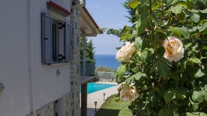 A stone-paved pathway leading to a building with a pool, surrounded by lush greenery and blooming roses. - Corinthian Residence (Xylokastro-Evrostina)