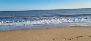 Una playa con arena y olas acercándose a la costa.