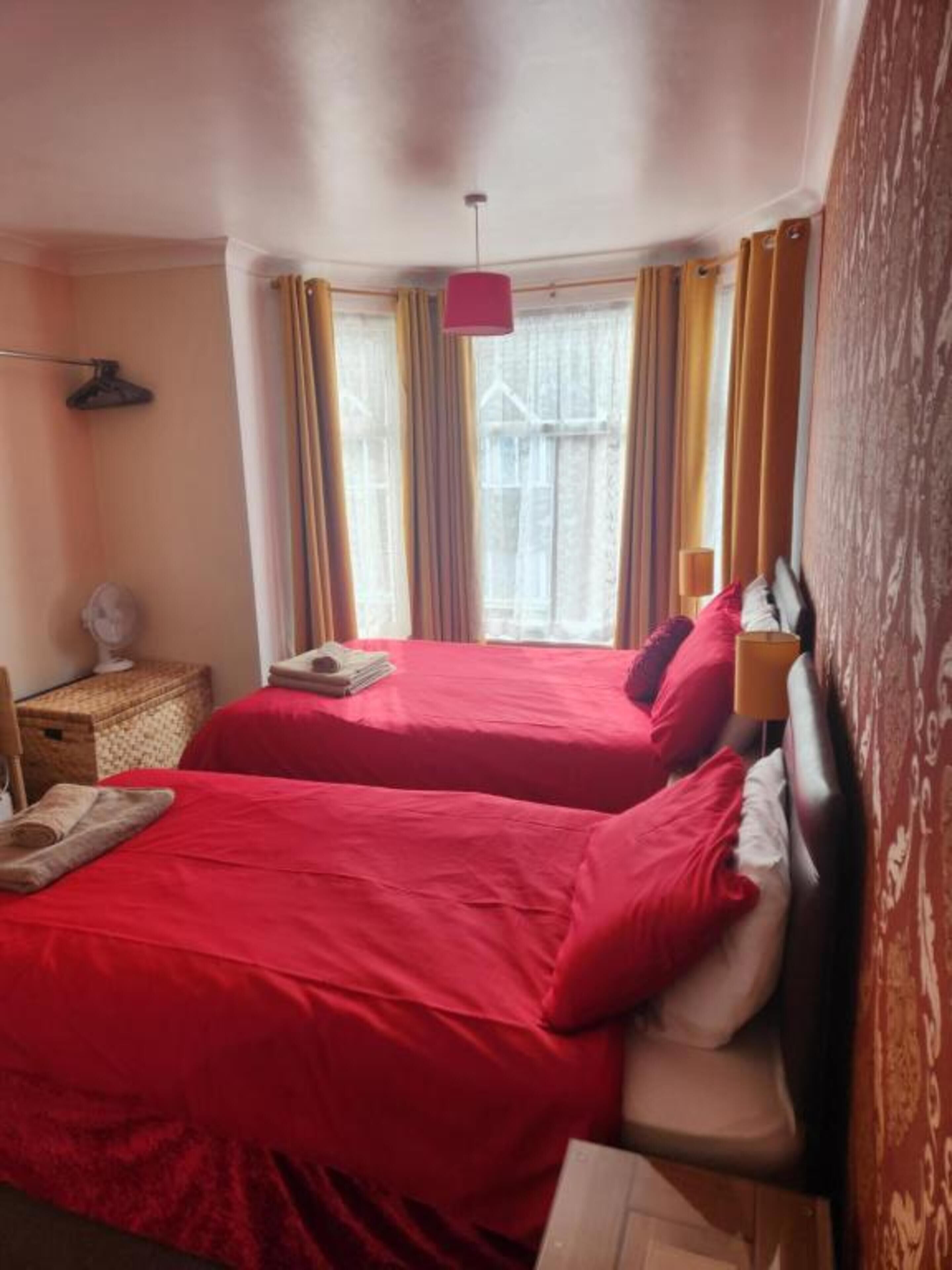 Quarto com duas camas, uma mesa de cabeceira, uma luminária e janela com cortinas.