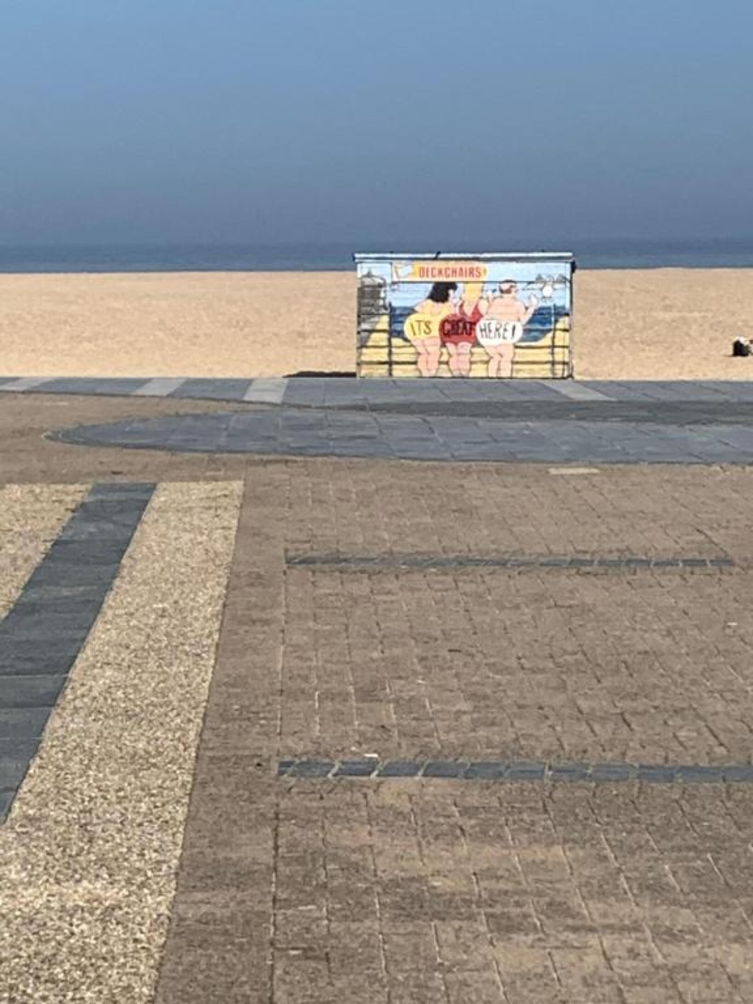 Une vue sur la plage avec un panneau publicitaire indiquant « DICKCHAIRS » et « C’EST GÉNIAL ICI ! »