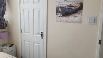 Um quarto com uma cama, uma porta, uma mesa de cabeceira, uma luminária e uma pintura de um barco na parede.
