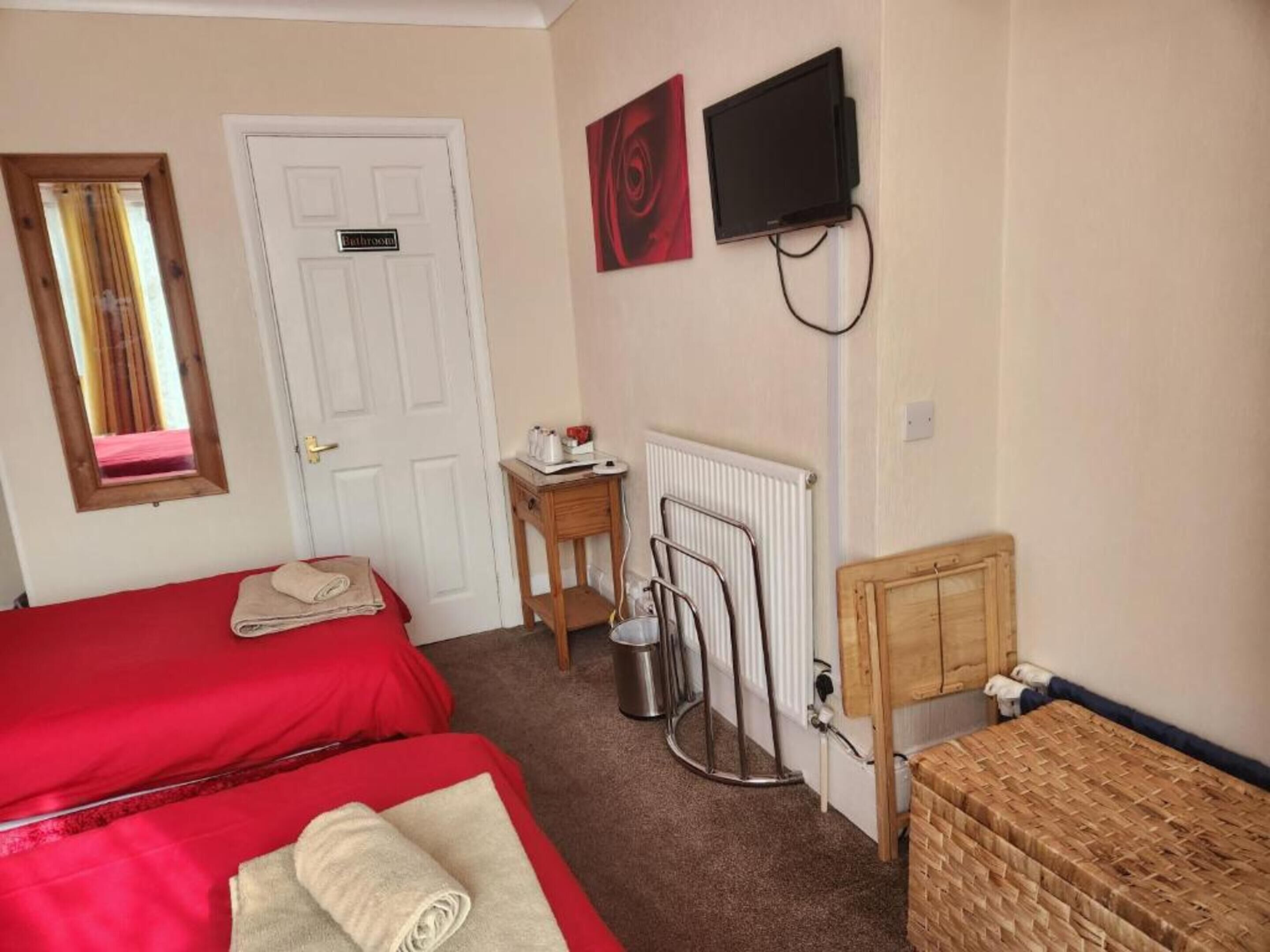 Une chambre avec deux lits, une petite table avec une bouilloire, un radiateur et un téléviseur fixé au mur.