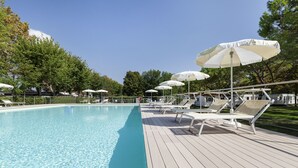 A swimming pool with clear water, surrounded by sun loungers and white umbrellas on a wooden deck. - Camping Fusina (Mestre)