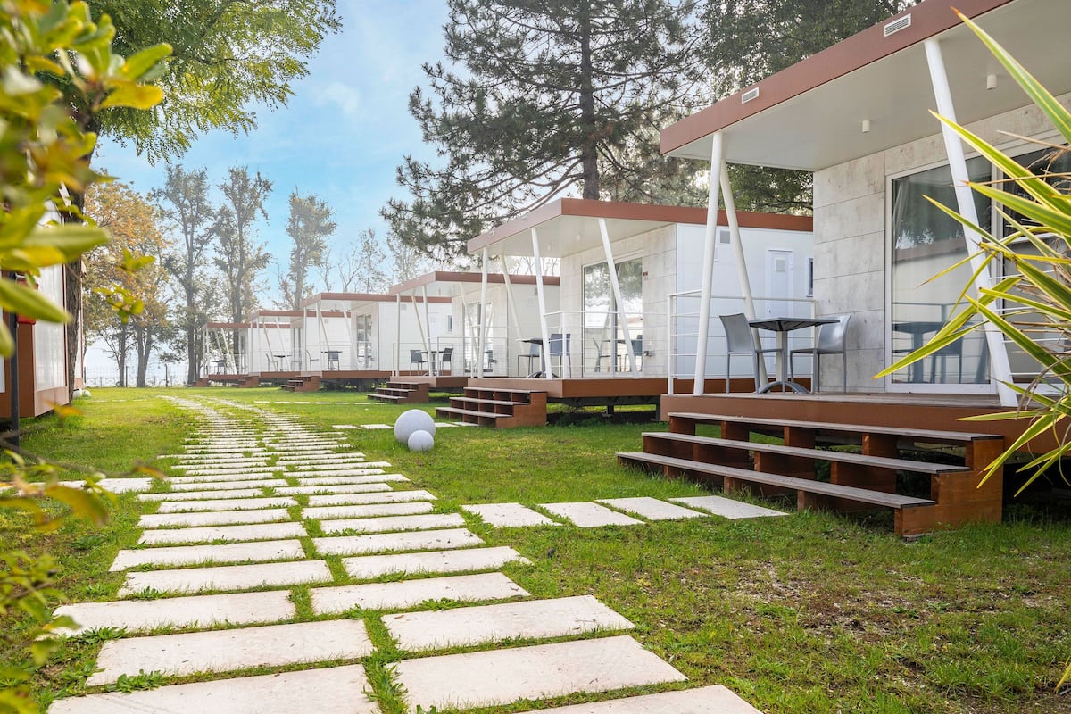 A row of modern, single-story cabins with outdoor seating areas and a stone pathway leading through a grassy area.