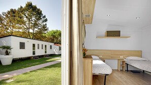 A modern, well-lit room with two beds, a small desk, and a view of a white mobile home in the background. - Camping Fusina (Mestre)