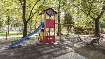 Explore the playground area surrounded by trees and a paved walkway, featuring a play structure with a slide and swing set.