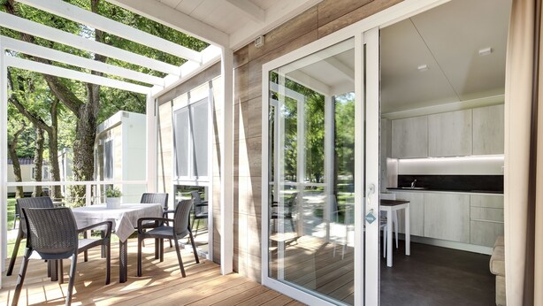 A covered outdoor patio with a table and chairs, a sliding glass door leading to a kitchen area. - Camping Fusina (Mestre)