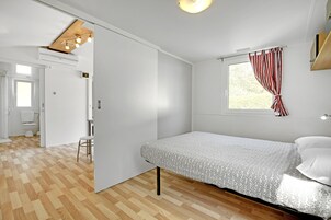 Une chambre à coucher avec un lit, une fenêtre avec des rideaux, une porte donnant sur une autre pièce et un luminaire au plafond.