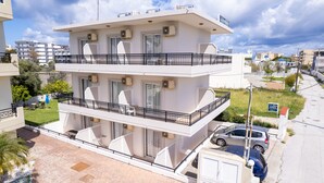 Un edificio residencial de varios pisos con balcones, unidades de aire acondicionado y un estacionamiento con automóviles.