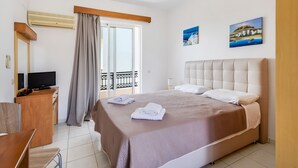 Habitación de hotel con cama, televisión, escritorio, silla, balcón con vistas y dos cuadros en la pared.
