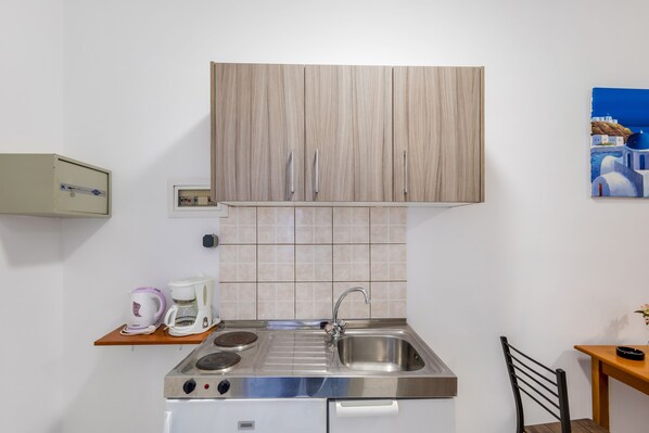A compact kitchen with a built-in stove, sink, and wooden cabinets. - Johnhara Studios & Apartments (Rhodes)