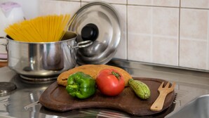 Una encimera de cocina con una olla de espagueti, una tabla de cortar de madera con un tomate, un pimiento verde y un calabacín.