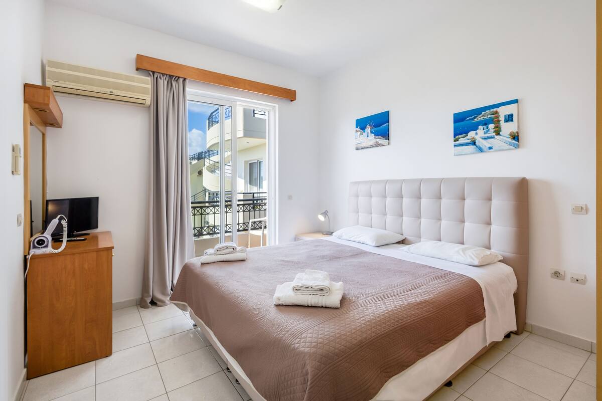 Habitación de hotel con una cama grande, televisión, escritorio con teléfono y balcón con vistas.