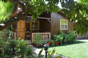 A wooden cabin with a porch, surrounded by potted plants and a well-maintained lawn. - Caretta Caretta Pension (Kemer)