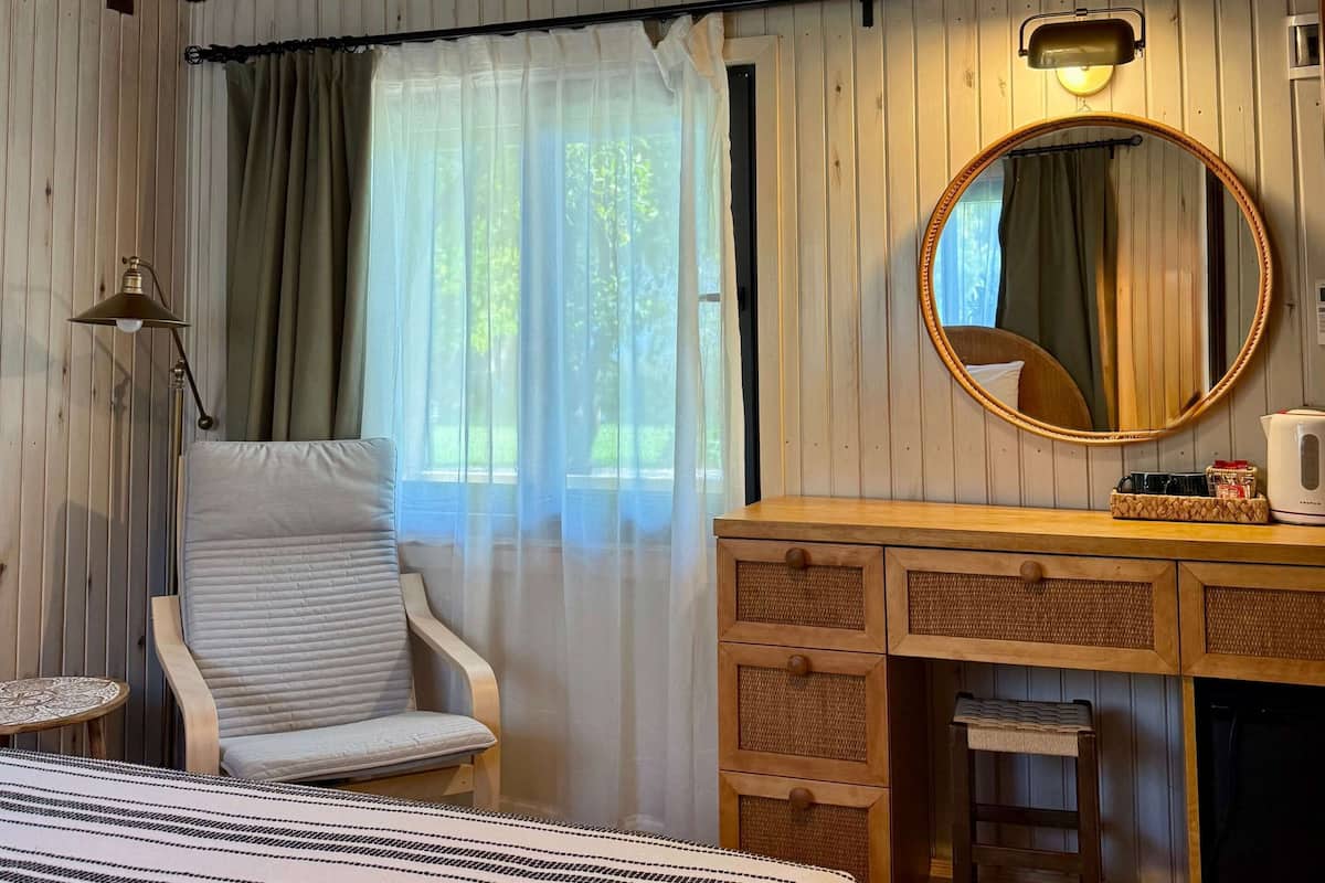 A room with a bed, a chair, a desk, a mirror, and a window with curtains.