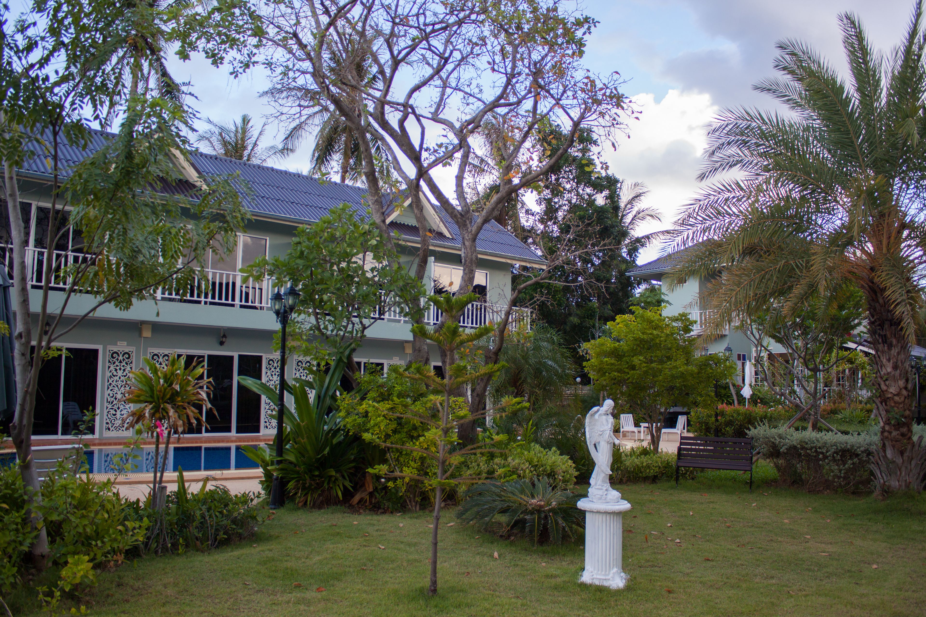 Uma casa com piscina, rodeada por vegetação exuberante e uma estátua.