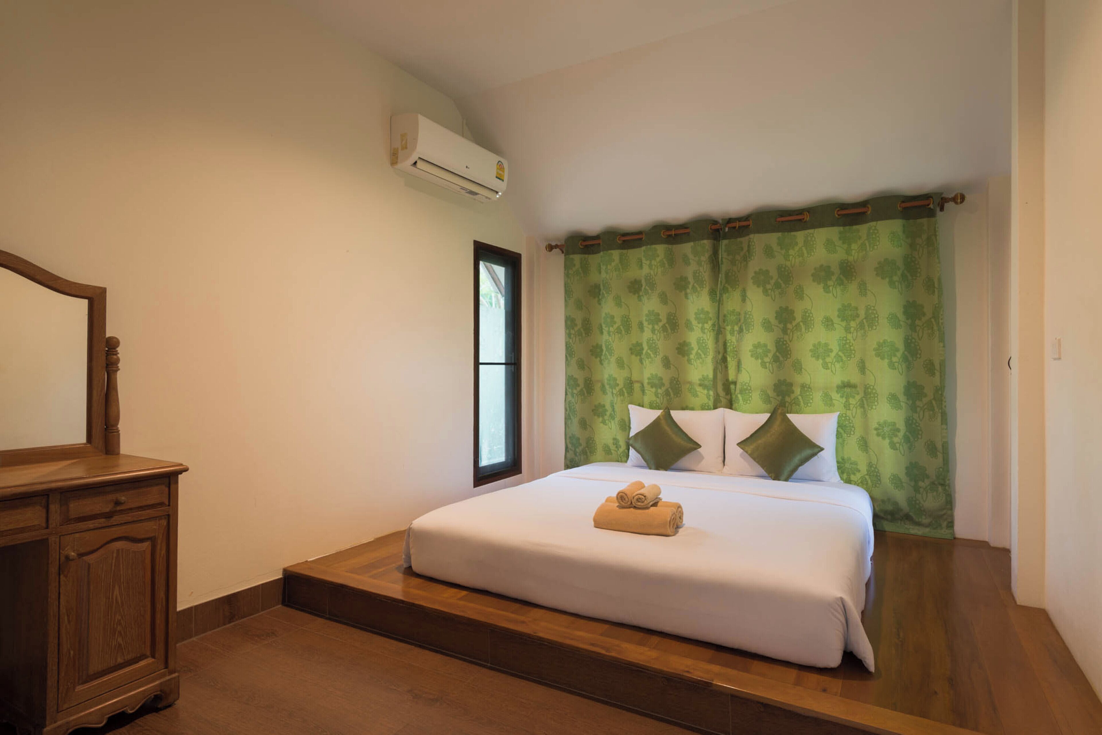 Une chambre avec une commode en bois, un lit avec des rideaux verts et un appareil de climatisation.