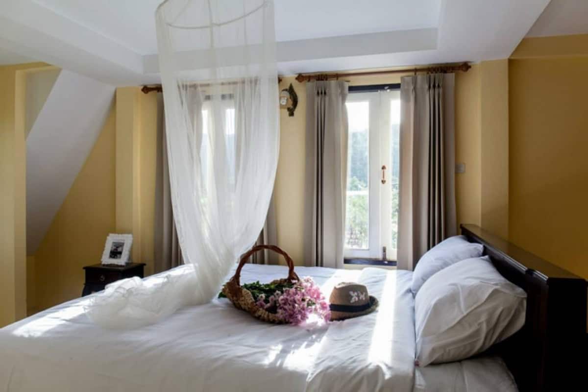 Ein Schlafzimmer mit Bett, Nachttisch, einem Fenster mit Vorhängen und Blick ins Grüne.