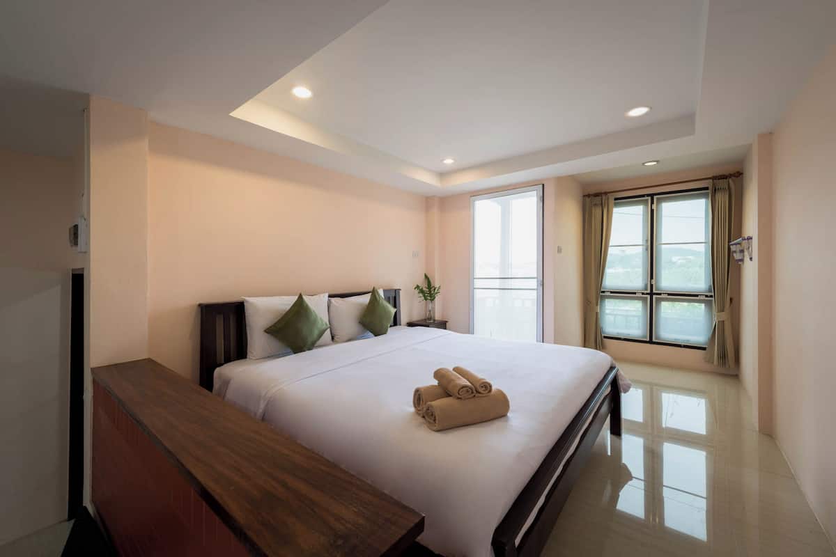 Ein modernes Hotelzimmer mit einem großen Bett, einer Holzbank, einem Fenster mit Vorhängen und einer Deckenleuchte.