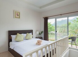 Camera d'albergo con un letto, un comodino, una finestra vista verde e un balcone con una sedia.