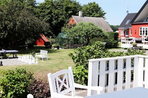 A garden area with a chessboard, a white bench, and a red building in the background. - Rosengaarden Hostel (Akirkeby)