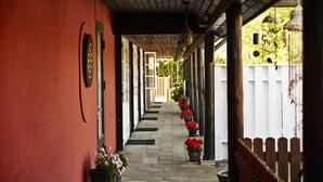 A covered corridor with a wooden ceiling, potted red flowers, and a white fence in the background. - Rosengaarden Hostel (Akirkeby)