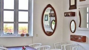 A dining area with a table and chairs, a window with a view of flowers, and several mirrors on the wall. - Rosengaarden Hostel (Akirkeby)