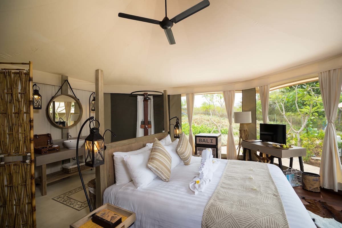 A bedroom with a bed, bedside table, TV, and a view of greenery.