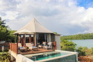 A secluded pool area with lounge chairs and a canopy, surrounded by lush greenery and a view of the water. - Menjangan Dynasty Resort (Pejarakan)