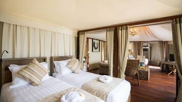 Quarto de hotel com duas camas, um espaço de estar com uma poltrona e mesa, e vista para o exterior.