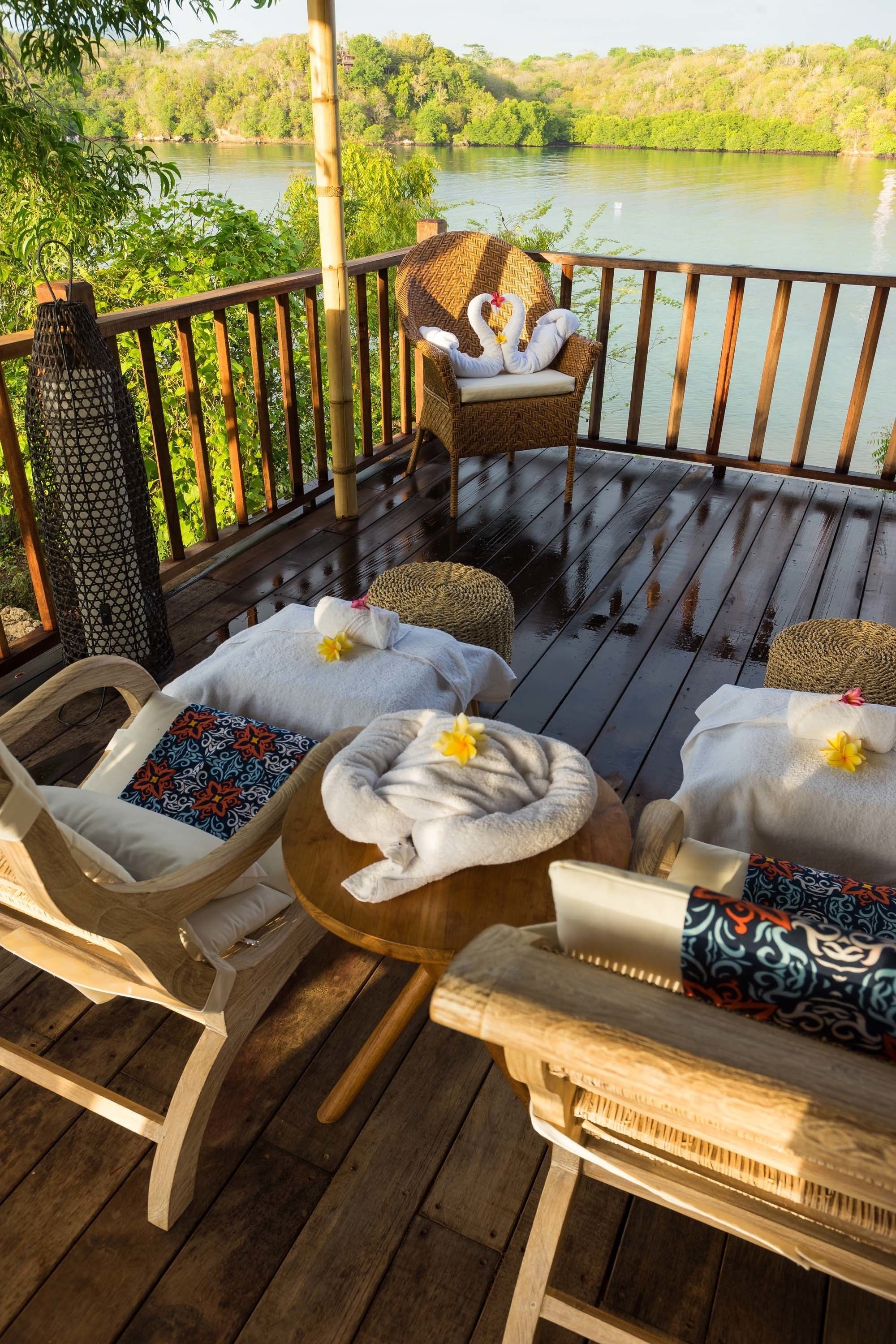 A wooden deck with wicker chairs and a table, each with a towel and flower.