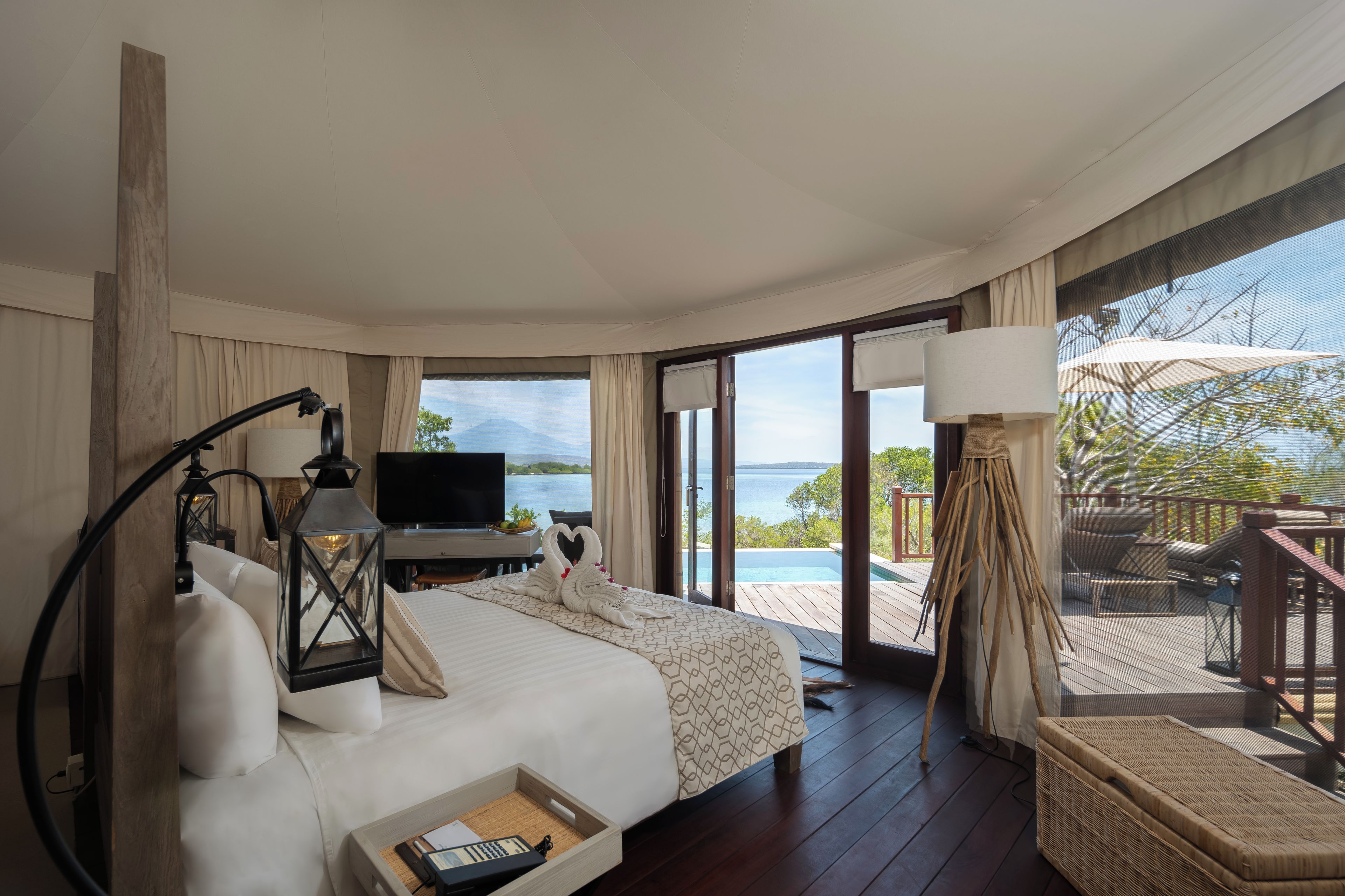 A hotel room with a bed, a desk, a television, and a view of the sea.