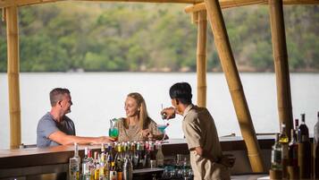 Zona de bar con estructura de bambú, botellas de licor y vista a un lago.