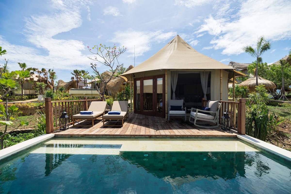 A poolside area with a wooden deck, lounge chairs, and a covered seating area.