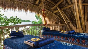 Una habitación con estructura de bambú y dos camas, cada una con ropa de cama azul y almohadones decorativos.