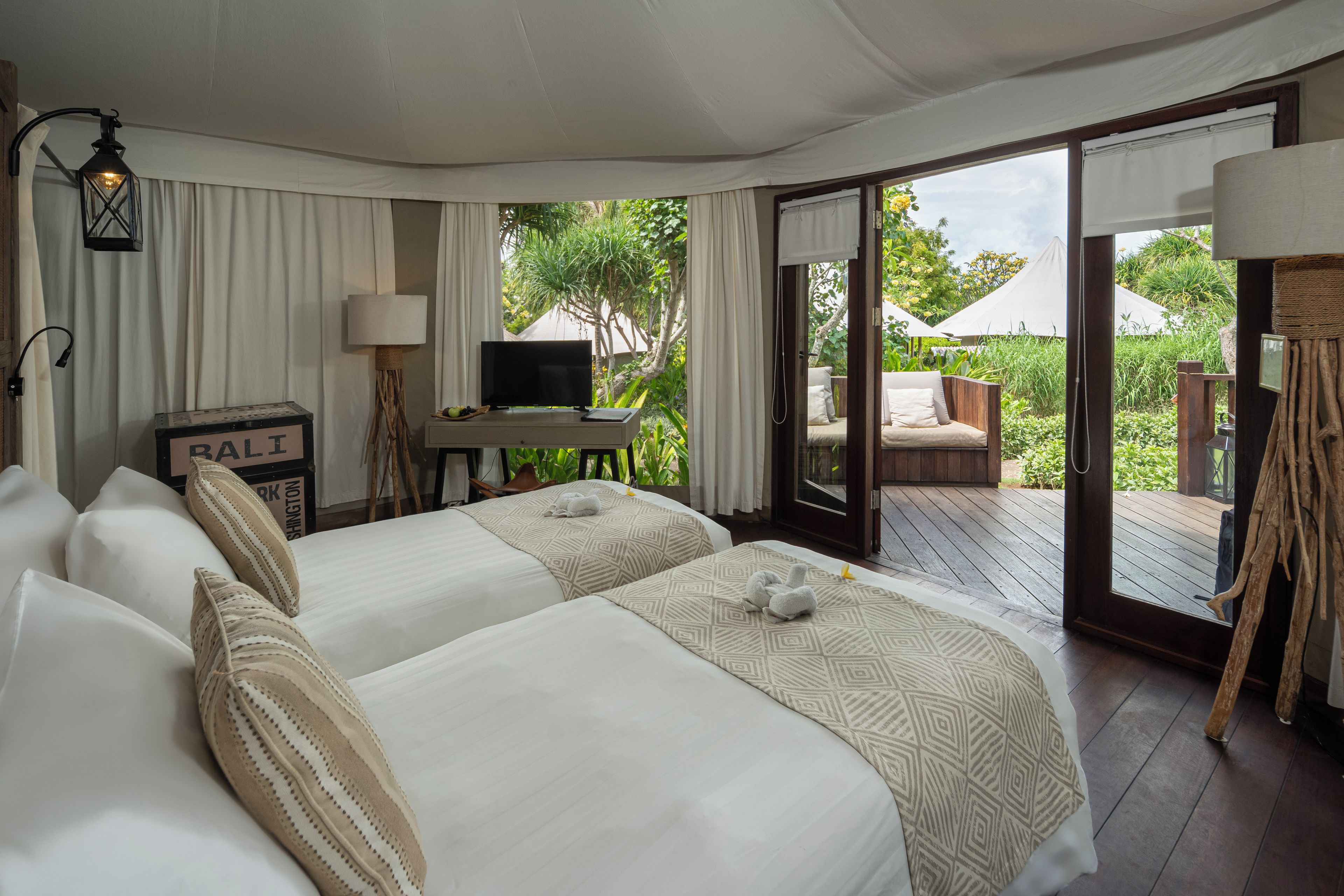 A hotel room with two beds, a desk with a television, and a sliding glass door leading to an outdoor area.
