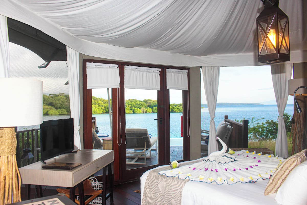 A bedroom with a bed, a desk, a television, and a view of the sea.