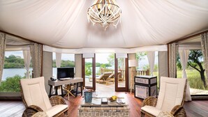 Una lujosa habitación con carpa, con un gran candelabro, muebles de mimbre, un televisor y vistas a un lago.