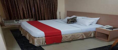 A hotel room with a bed, a nightstand, a telephone, and a window with curtains.