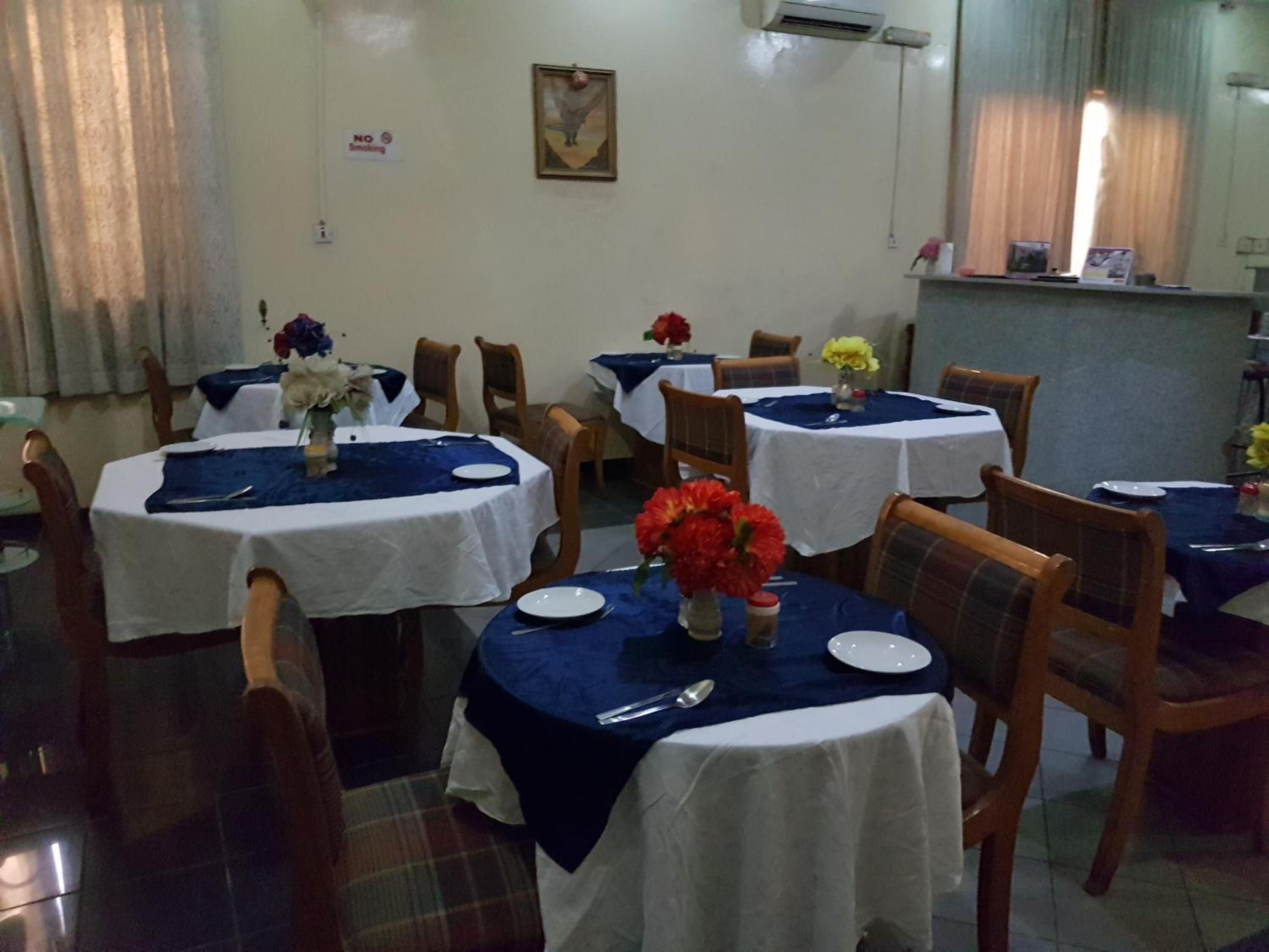 Un espace repas avec des tables rondes recouvertes de nappes blanches et de sets de table bleus, des chaises en bois et des centres de table floraux.