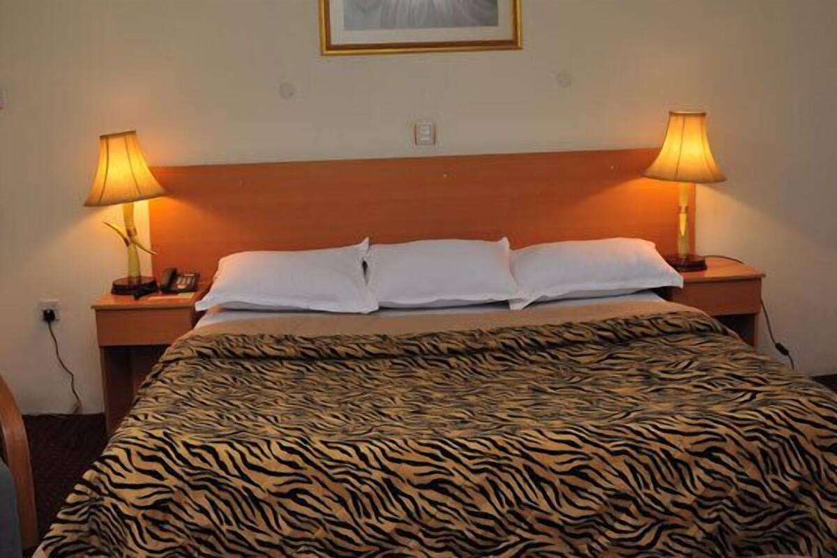 A hotel room with a bed, two bedside lamps, a chair, and a framed picture on the wall.