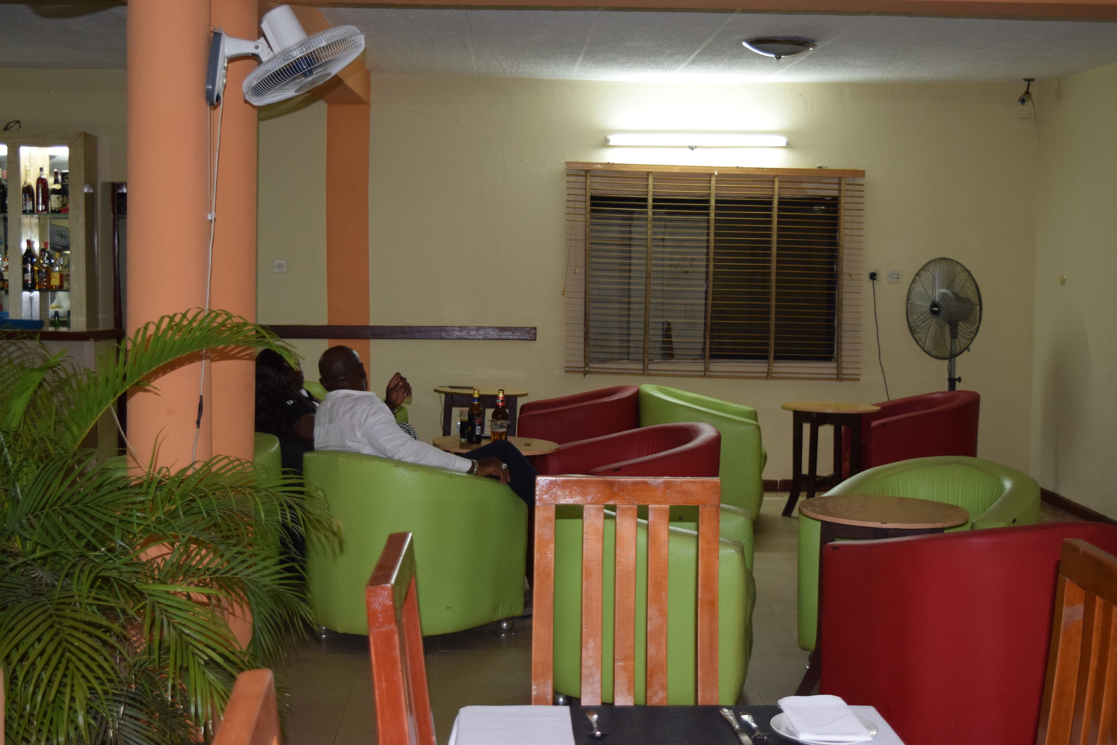 A seating area with green and red chairs, a table with a black tablecloth, and a fan on the wall.