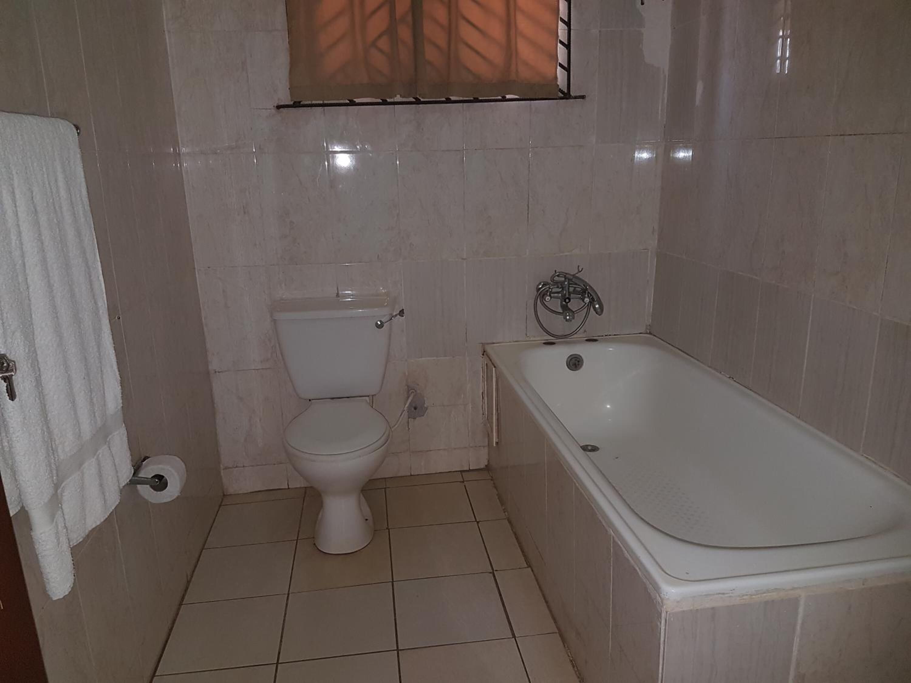 A bathroom with a toilet, a bathtub, and a window with blinds.