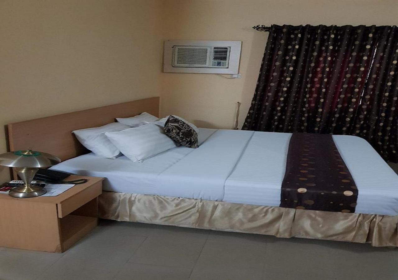 Ein Hotelzimmer mit Bett, Nachttisch, Klimaanlage und Vorhang.