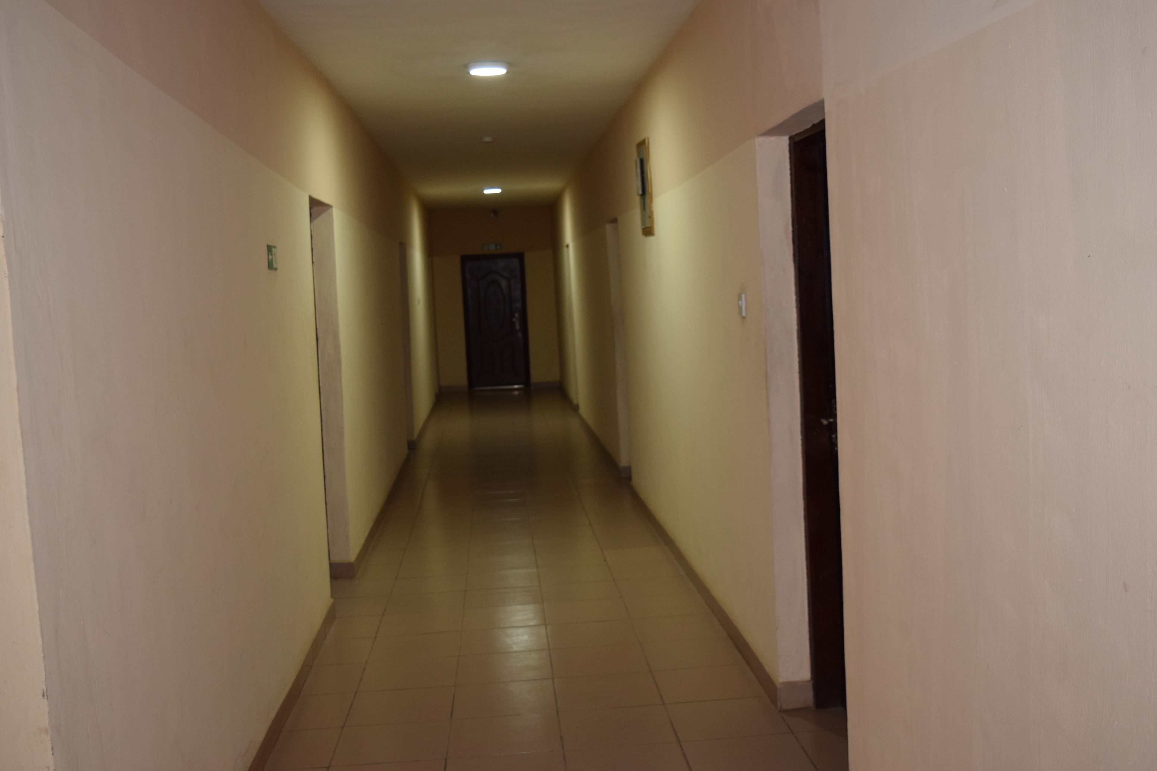 Un pasillo largo y estrecho con puertas a ambos lados, que conduce a una puerta oscura al final.