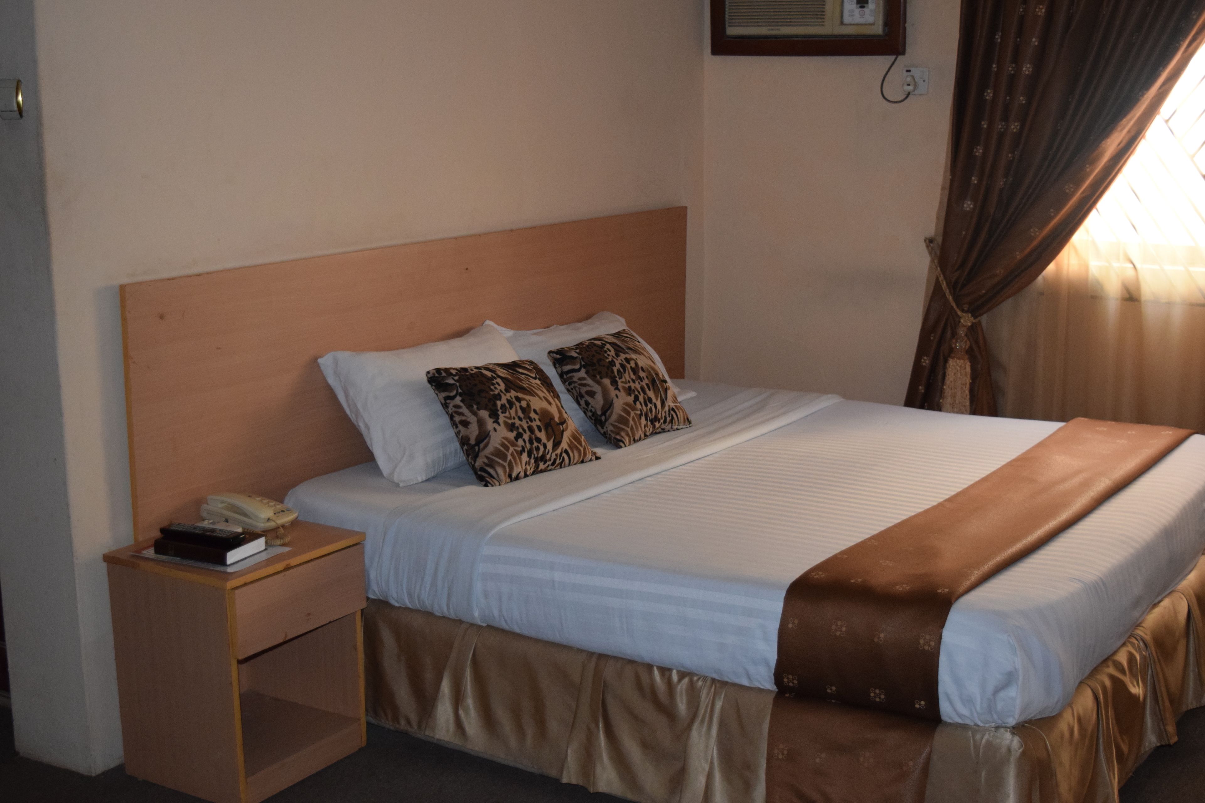 A neatly made bed with a wooden headboard, two patterned pillows, and a bedside table with a telephone and book.