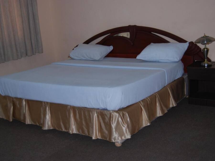 Una habitación de hotel estándar con una cama individual, una mesita de noche y una lámpara.