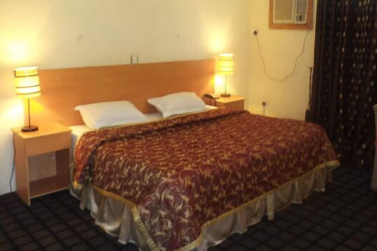 A hotel room with a bed, two bedside lamps, a chair, and a window with curtains.
